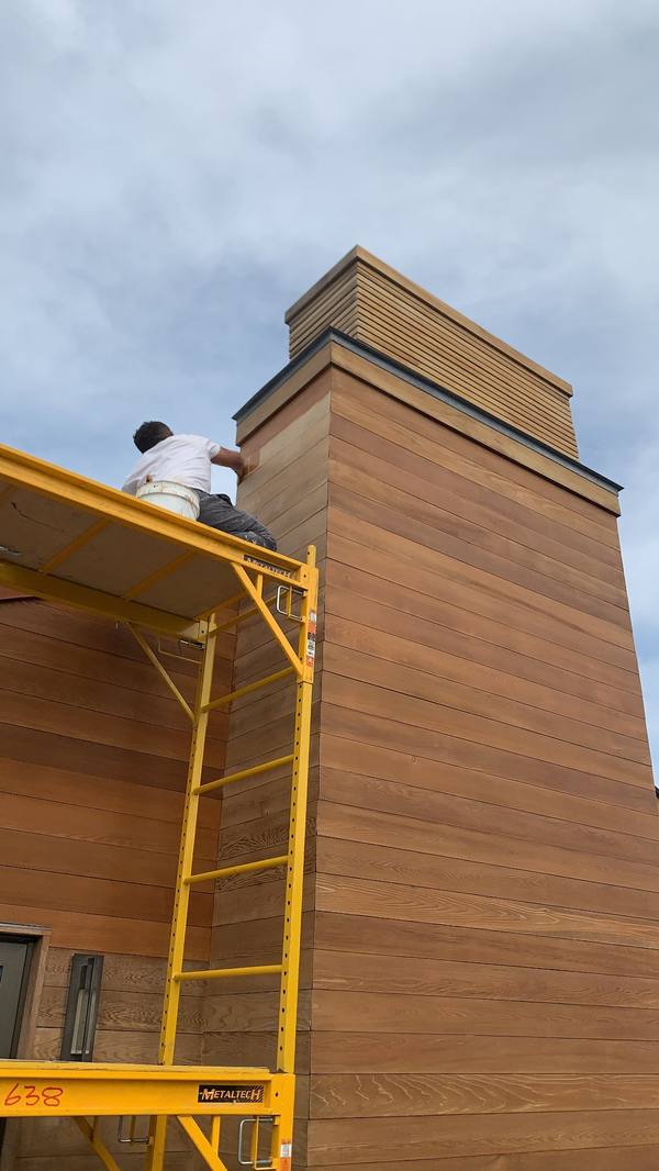 Painter staining the cedar siding of a chimney from scaffolding in the Hamptons