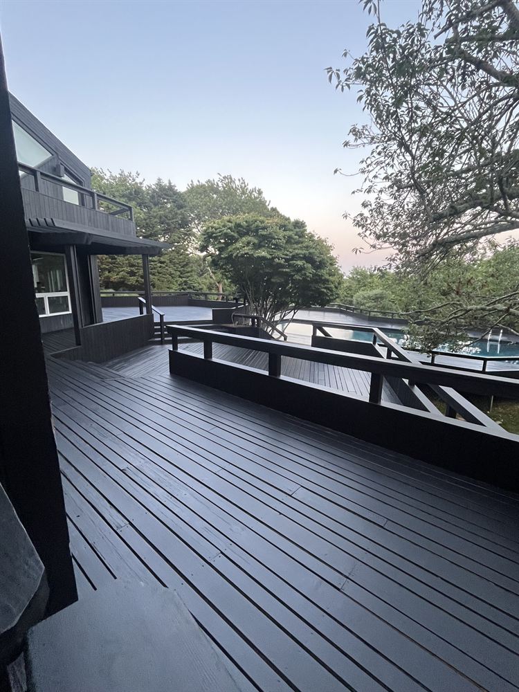 Refinished black wraparound deck with built-in benches beside a pool